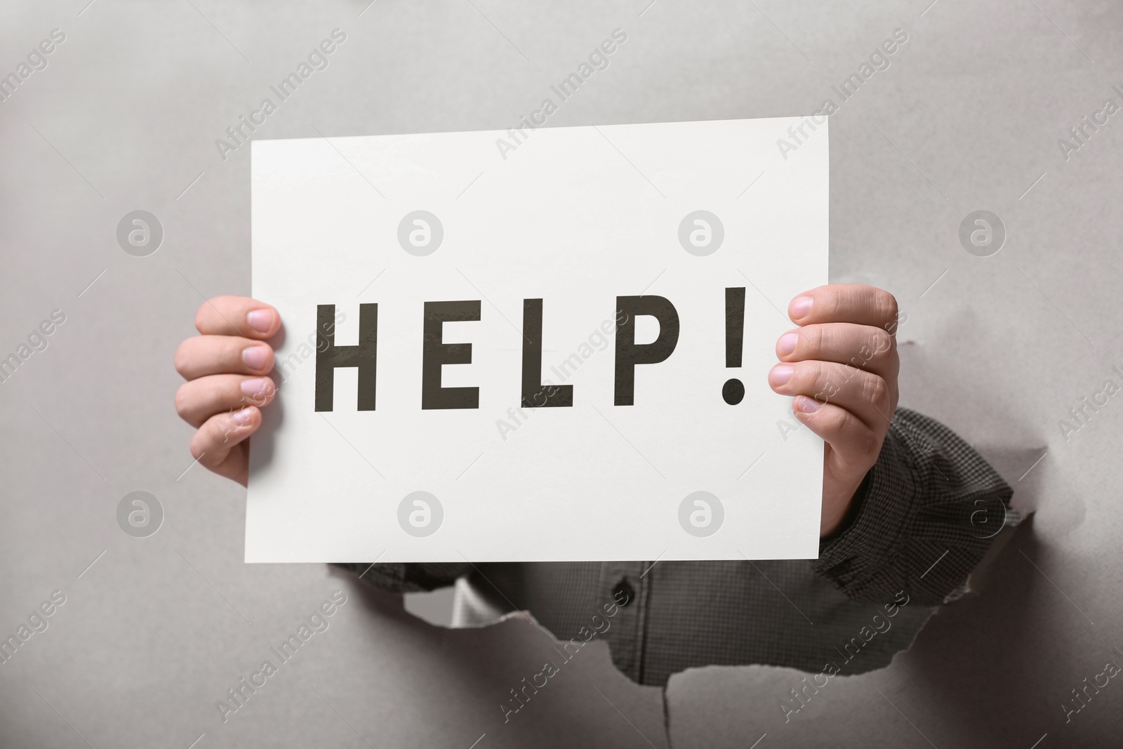 Image of Man holding paper with word Help through hole in grey paper, closeup
