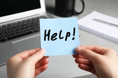 Image of Woman holding paper note with word Help at workplace, closeup