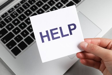 Image of Woman holding paper note with word Help above laptop, closeup