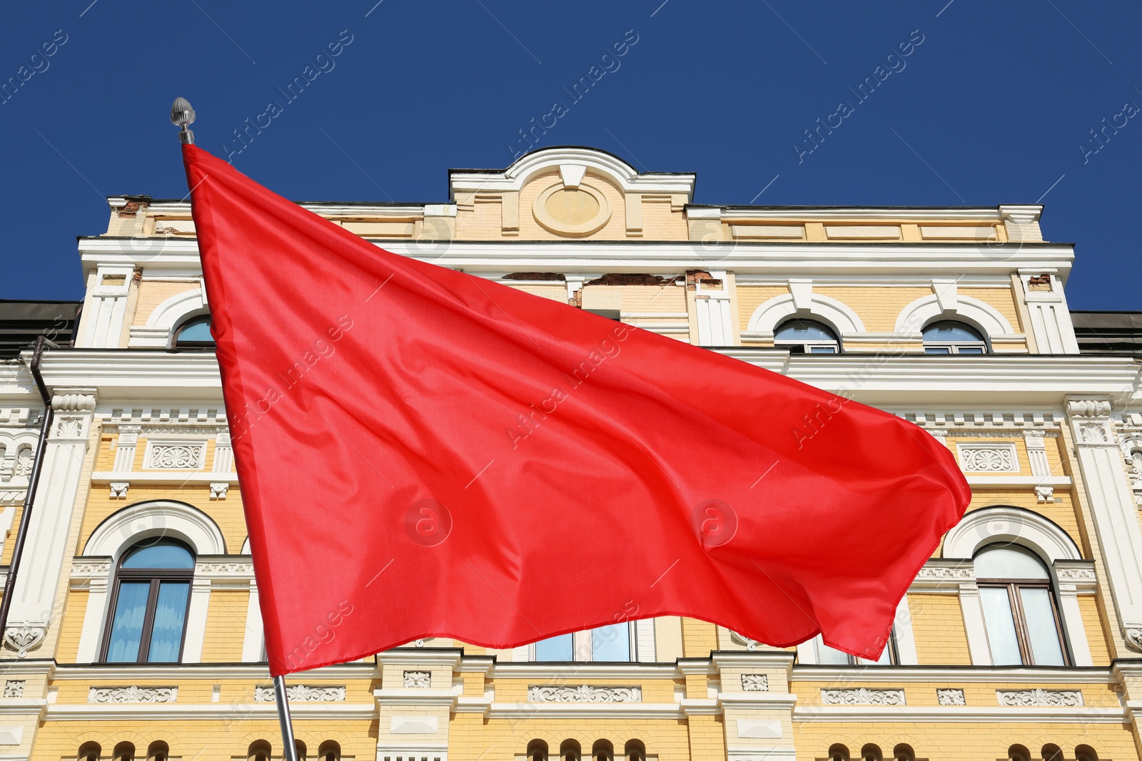 Bright red flag waving against building outdoors Image of Bright red flag waving against building outdoors