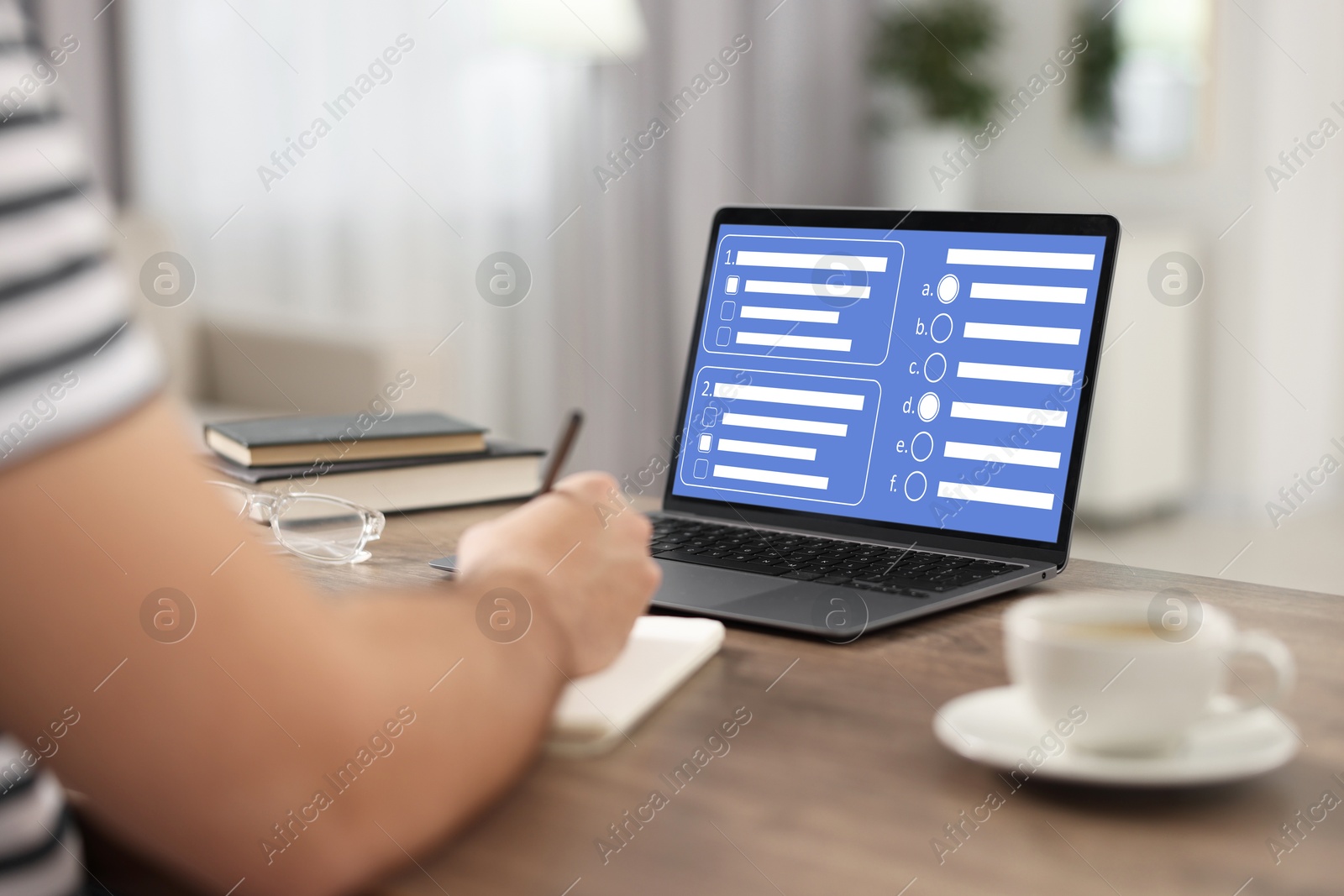 Image of Man passing online test on laptop and writing in notebook at table, closeup
