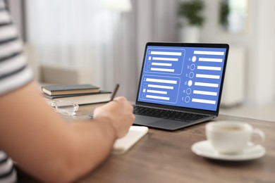 Image of Man passing online test on laptop and writing in notebook at table, closeup