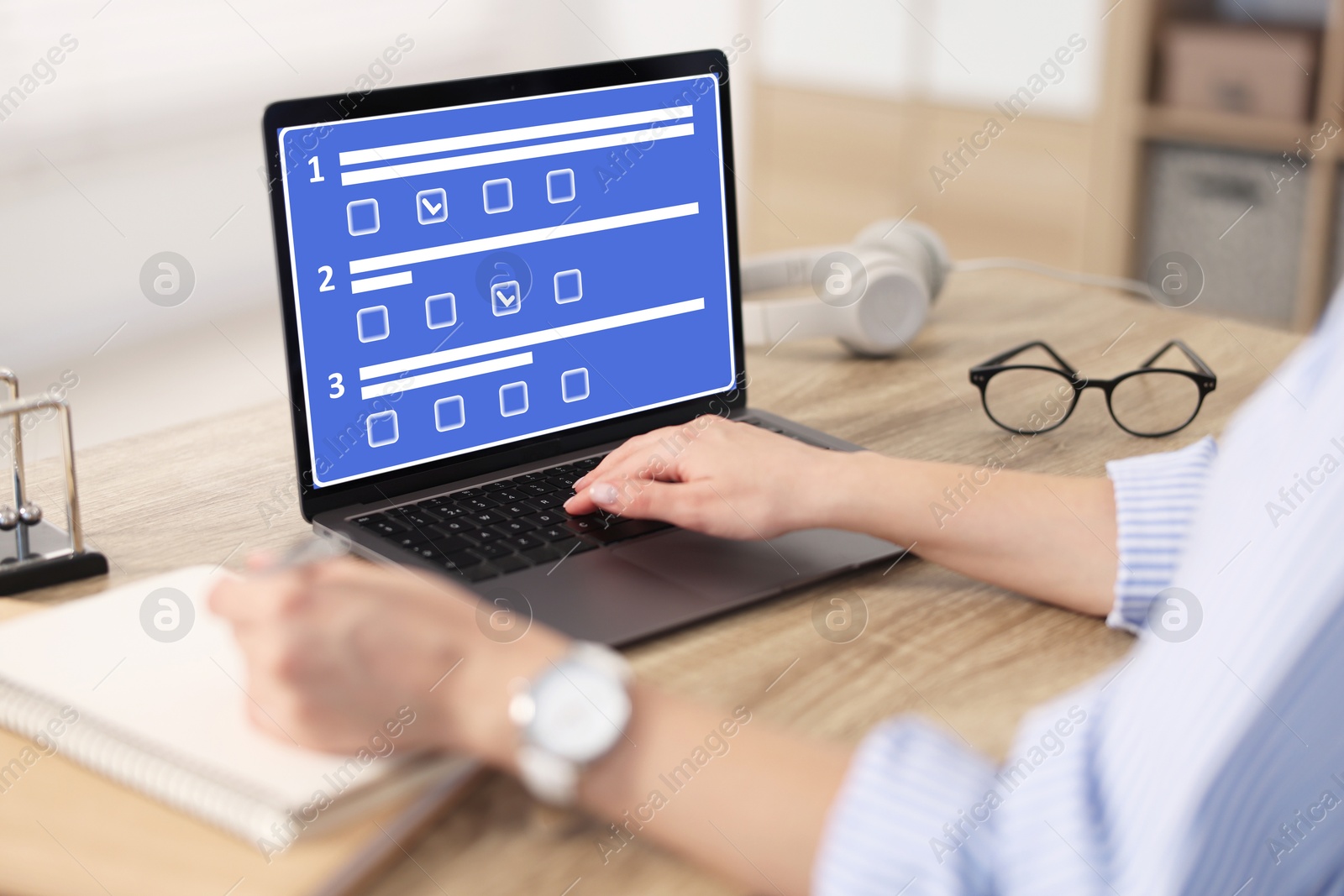 Image of Woman passing online test on laptop and writing in notebook at table, closeup