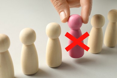 Image of Dismissal. Woman taking pink human figure with red cross away on light background, closeup