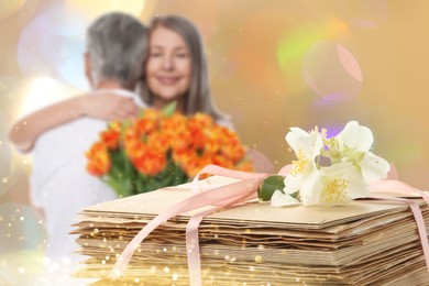 Image of Romantic senior couple and stack of love letters, bokeh effect. Woman with bouquet hugging her beloved man