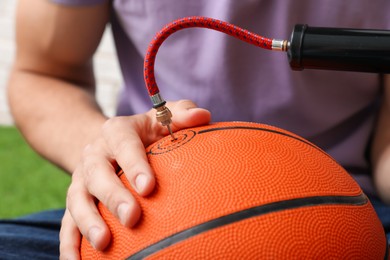 Photo of Man inflating basketball ball with manual air pump indoors, closeup