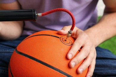 Photo of Man inflating basketball ball with manual air pump indoors, closeup