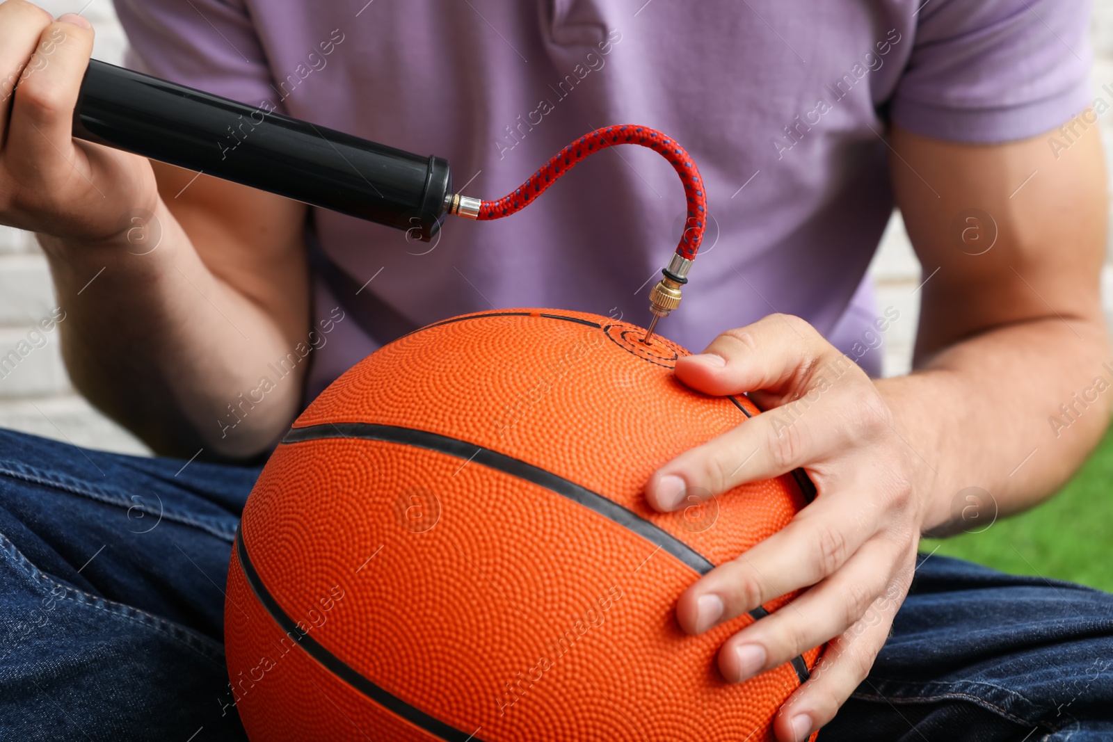 Photo of Man inflating basketball ball with manual air pump indoors, closeup