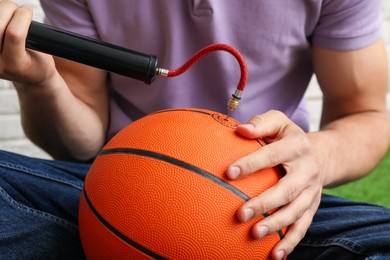 Photo of Man inflating basketball ball with manual air pump indoors, closeup