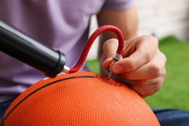 Photo of Man inflating basketball ball with manual air pump indoors, closeup