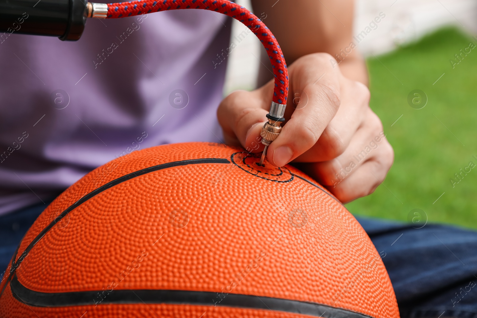 Photo of Man inflating basketball ball with manual air pump indoors, closeup