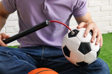 Photo of Man inflating soccer ball with manual air pump indoors, closeup