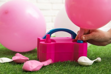 Photo of Woman inflating balloon with air pump indoors, closeup