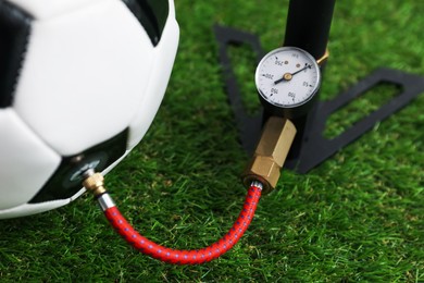 Photo of Soccer ball and manual air pump on artificial grass, closeup