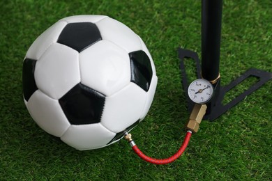 Photo of Soccer ball and manual air pump on artificial grass, closeup