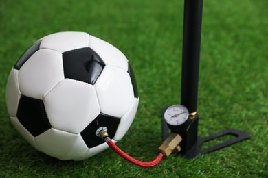Photo of Soccer ball and manual air pump on artificial grass, closeup