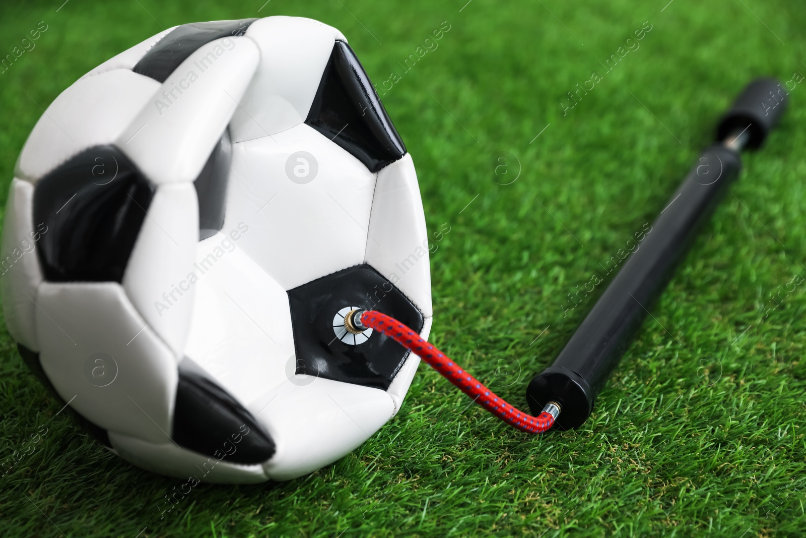 Photo of Soccer ball and manual air pump on artificial grass, closeup