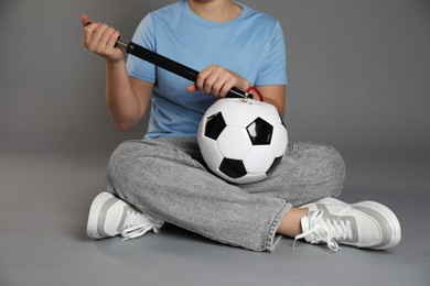 Photo of Woman inflating soccer ball with manual air pump on grey background, closeup