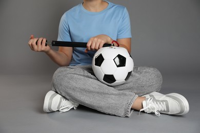 Photo of Woman inflating soccer ball with manual air pump on grey background, closeup