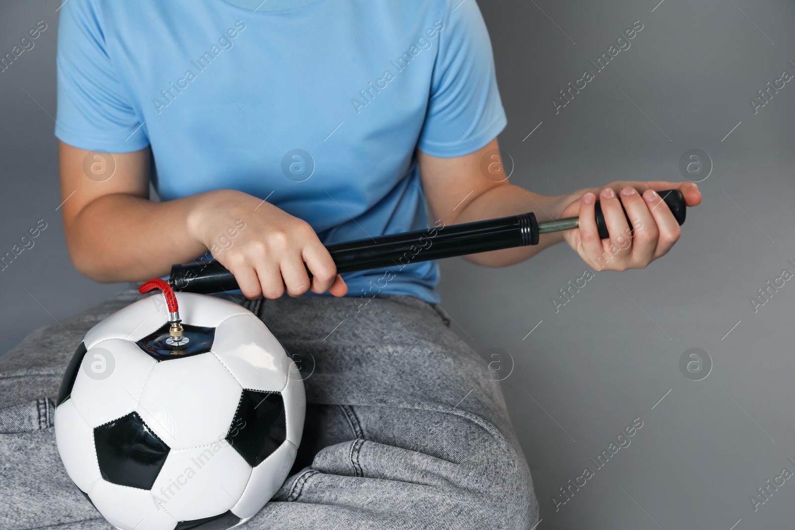 Photo of Woman inflating soccer ball with manual air pump on grey background, closeup