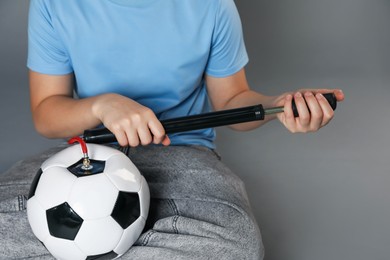 Photo of Woman inflating soccer ball with manual air pump on grey background, closeup