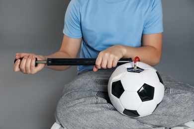 Photo of Woman inflating soccer ball with manual air pump on grey background, closeup