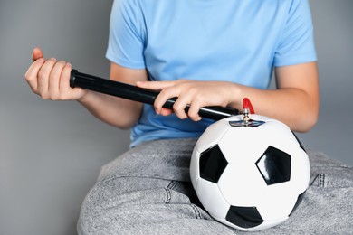 Photo of Woman inflating soccer ball with manual air pump on grey background, closeup