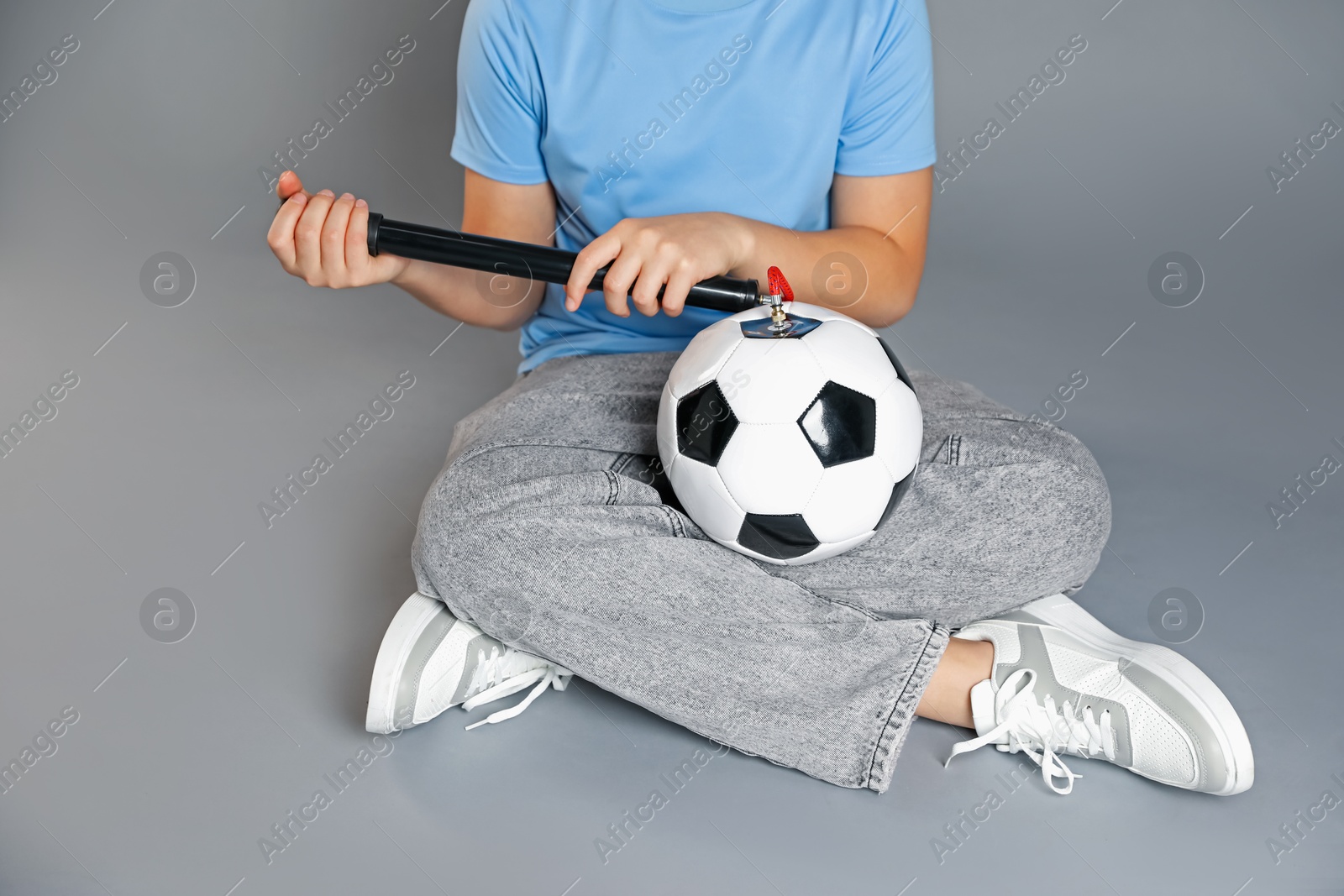 Photo of Woman inflating soccer ball with manual air pump on grey background, closeup