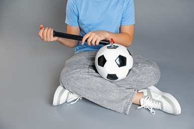 Photo of Woman inflating soccer ball with manual air pump on grey background, closeup