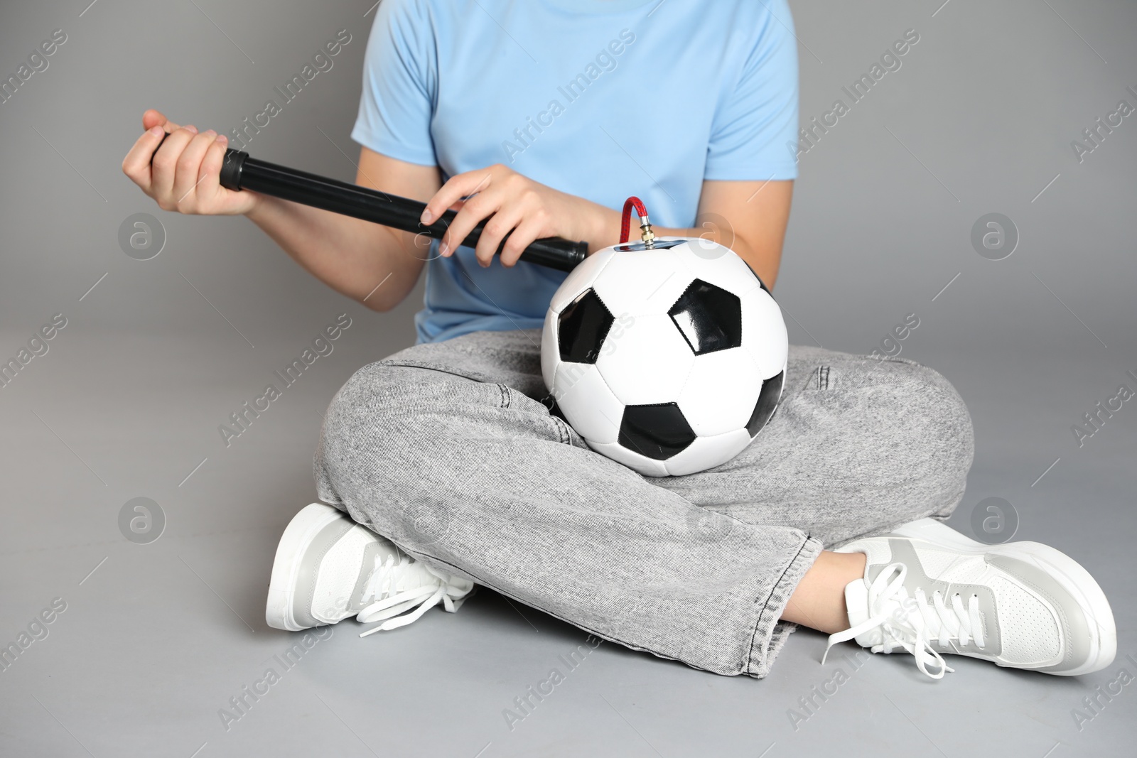 Photo of Woman inflating soccer ball with manual air pump on grey background, closeup