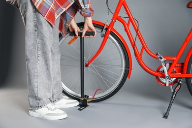 Photo of Woman inflating bicycle tire with manual air pump on grey background, closeup