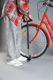 Photo of Woman inflating bicycle tire with manual air pump on grey background, closeup