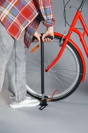 Photo of Woman inflating bicycle tire with manual air pump on grey background, closeup