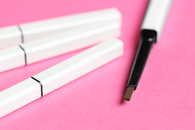Photo of Twist up eyebrow pencils on bright pink background, closeup