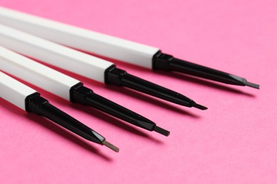 Photo of Twist up eyebrow pencils on bright pink background, closeup