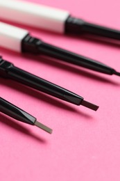Photo of Twist up eyebrow pencils on bright pink background, closeup