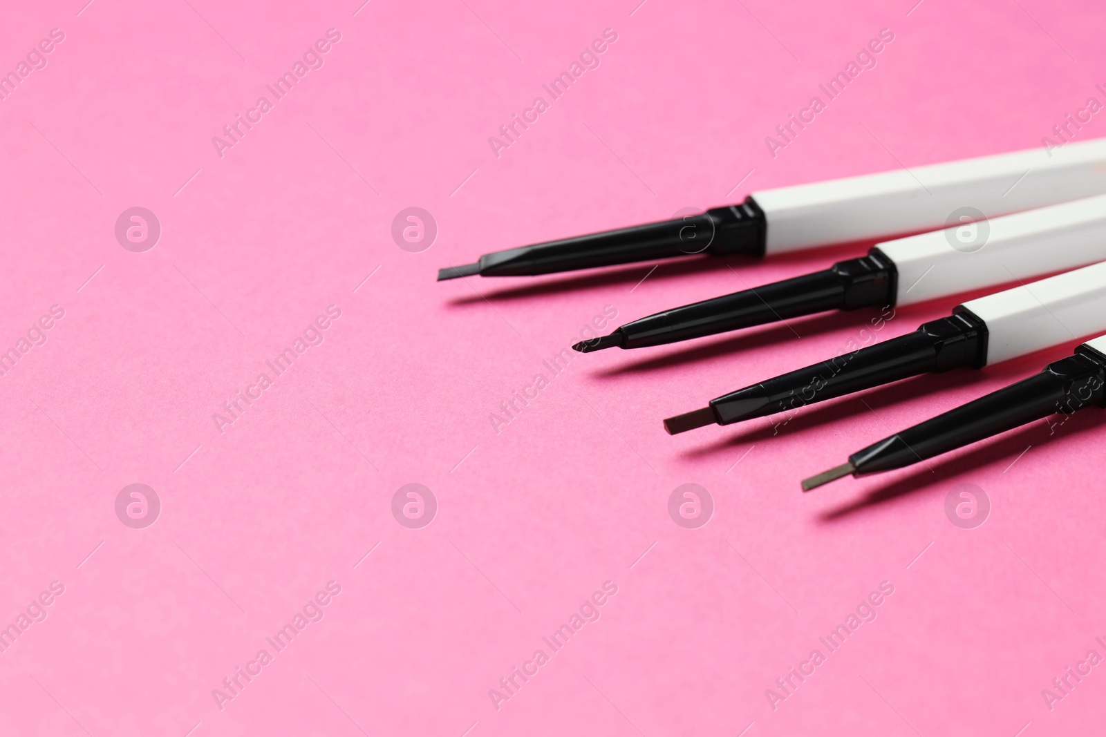 Twist up eyebrow pencils on bright pink background, closeup. Space for text Photo of Twist up eyebrow pencils on bright pink background, closeup. Space for text