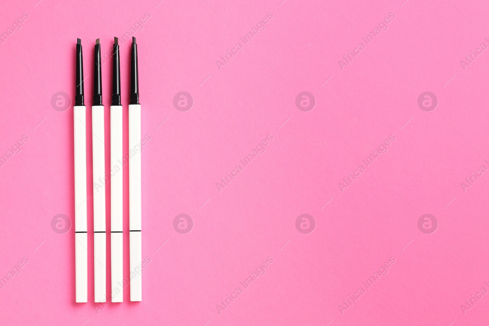 Twist up eyebrow pencils on bright pink background, flat lay. Space for text Photo of Twist up eyebrow pencils on bright pink background, flat lay. Space for text