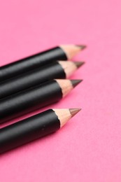 Photo of Different eyebrow pencils on bright pink background, closeup