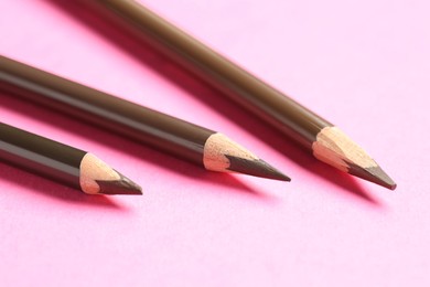 Photo of Different eyebrow pencils on bright pink background, closeup