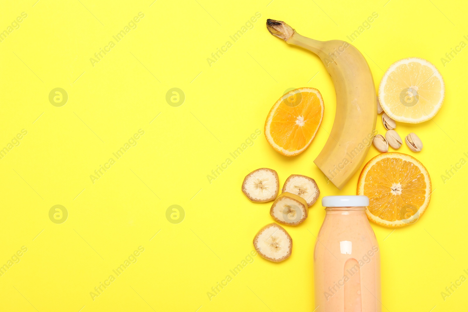 Photo of Superfood. Tasty smoothie in glass bottle and ingredients on yellow background, flat lay. Space for text