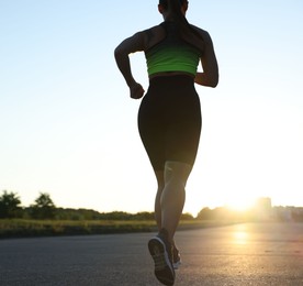 Photo of Woman in sportswear running on road outdoors, closeup