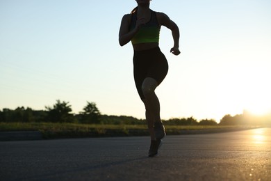 Photo of Woman in sportswear running on road outdoors, closeup