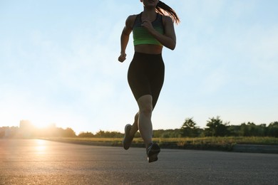 Photo of Woman in sportswear running on road outdoors, closeup