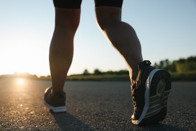 Photo of Woman in sneakers running on road outdoors, closeup