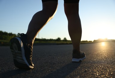 Photo of Woman in sneakers running on road outdoors, closeup