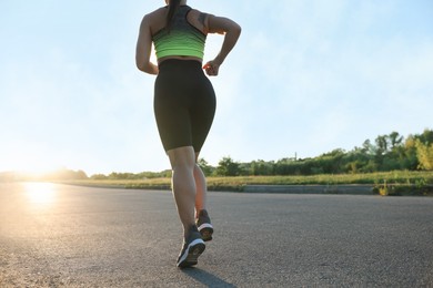 Photo of Woman in sportswear running on road outdoors, closeup