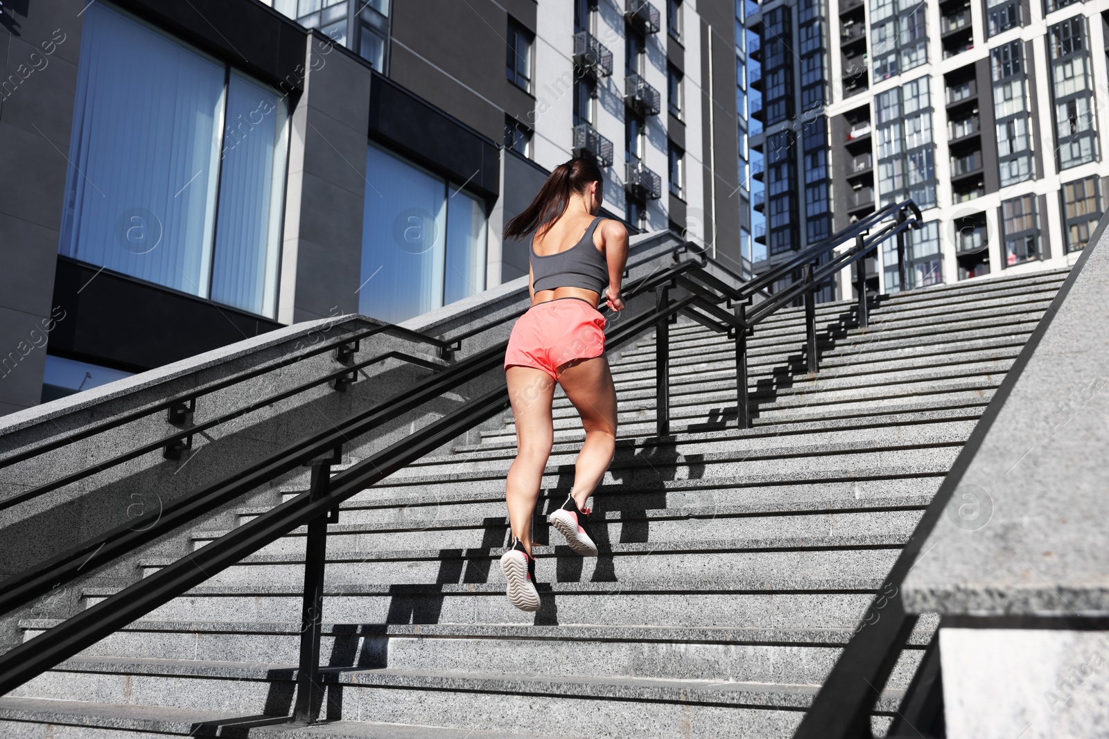Woman in sportswear running up on stairs outdoors, low angle view Photo of Woman in sportswear running up on stairs outdoors, low angle view