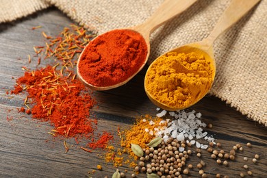 Photo of Different aromatic spices in spoons on wooden table, closeup