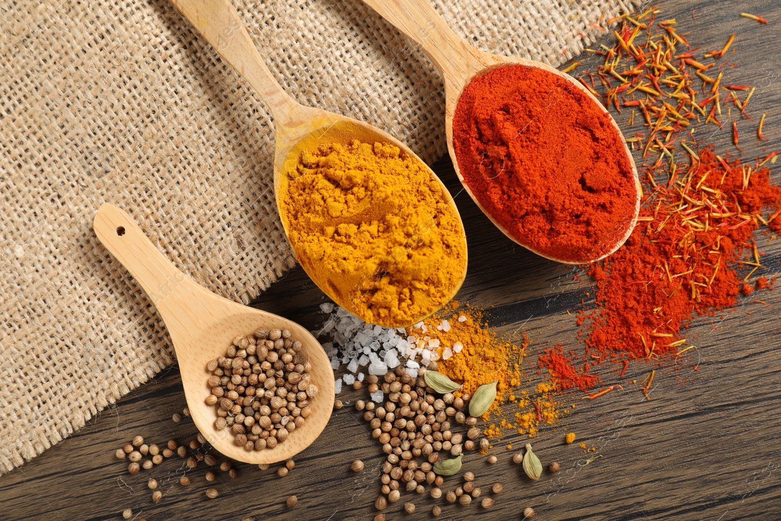 Photo of Different aromatic spices in spoons on wooden table, flat lay